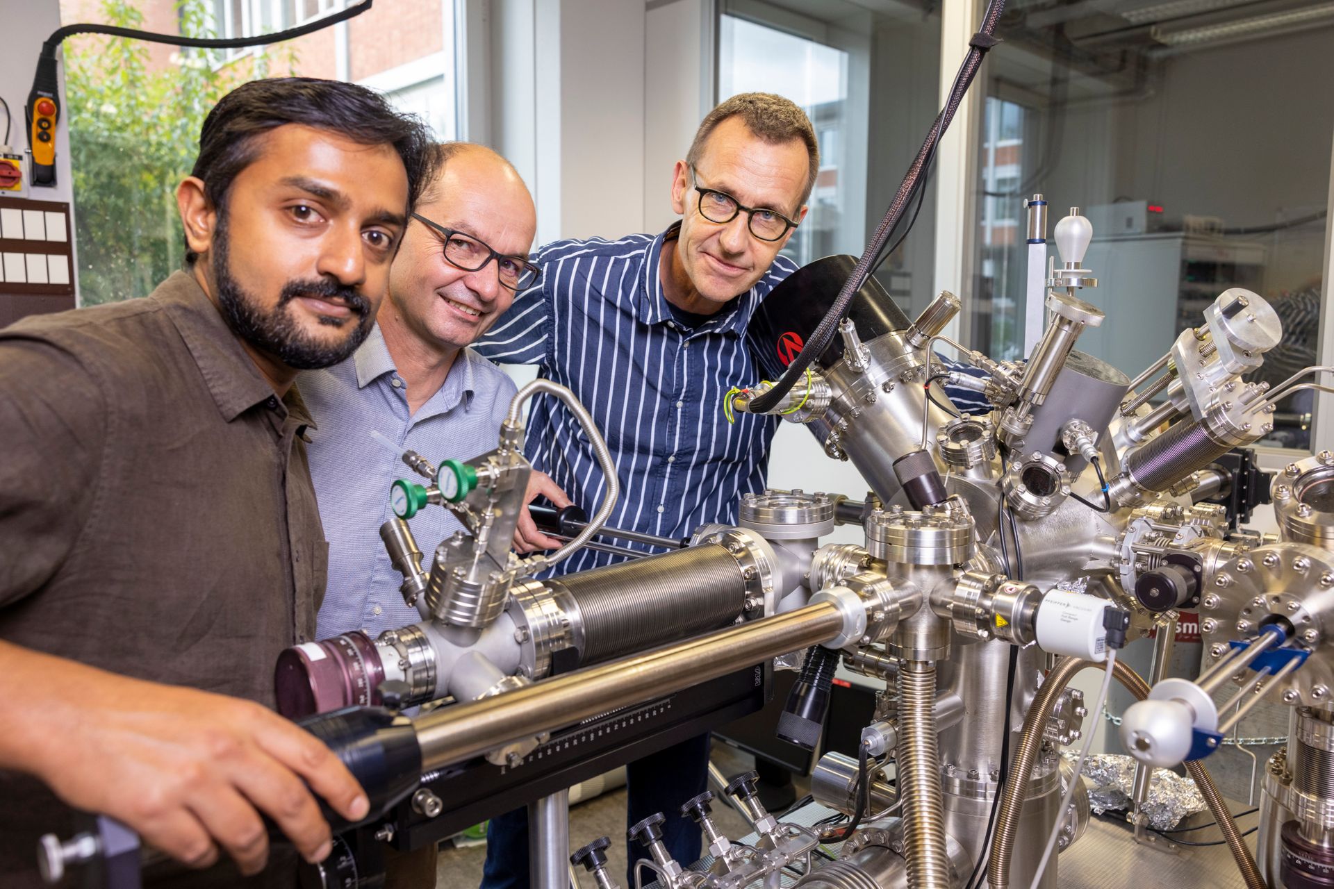 I ricercatori Shantanu Mishra, Pascal Ruffieux e Roman Fasel dell'EMPA accanto a un impianto per la creazione di vuoto ultraspinto, all’interno del quale è avvenuta la preparazione di catene di spin di Triangulene (Foto: Gian Vaitl/EMPA)