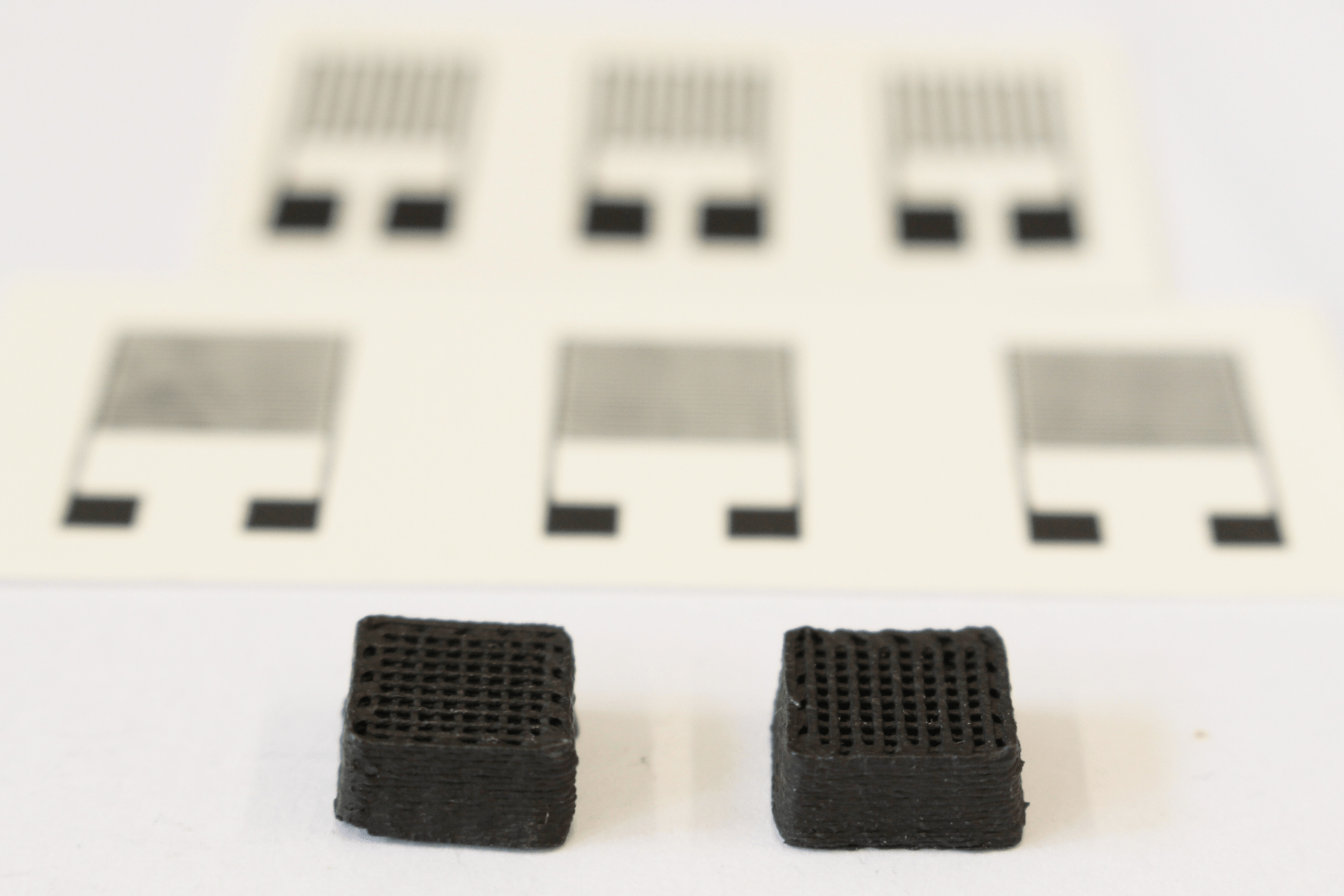 A new material for printed circuit boards derived from cochineal droppings: two centimeter-wide test cuboids made on a three-dimensional printer. Printed electronic sensors can be seen in the background (Photo: EMPA)