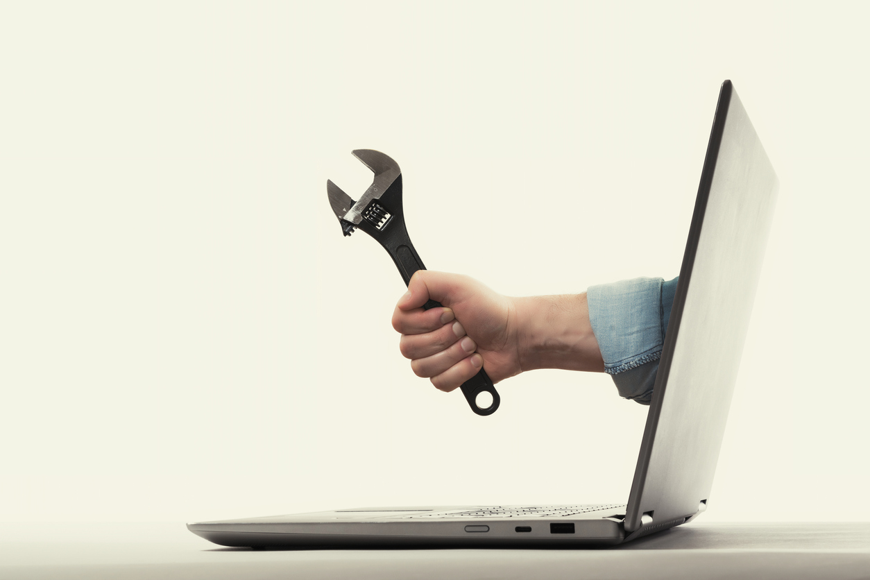 A wrench emerges from the screen of a laptop branded in one hand: this is an excellent metaphor for the concept of remote technical support
