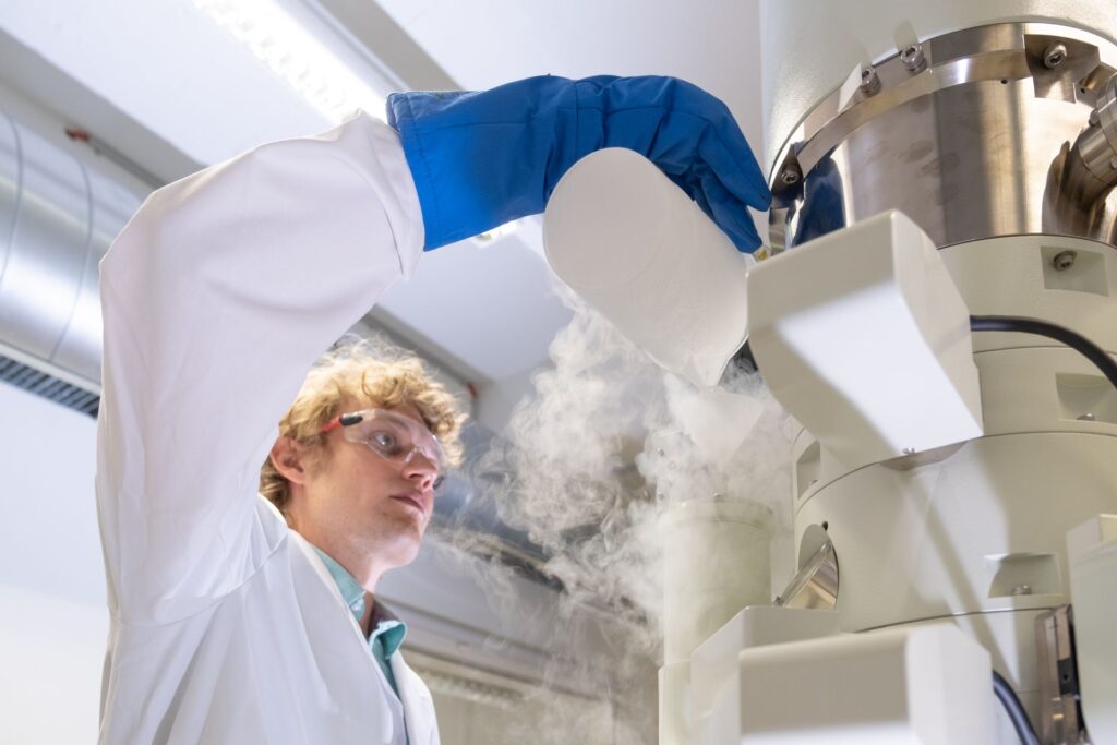 Fuoco e ghiaccio: Lukas Gerken, ricercatore dell'EMPA a San Gallo, produce nanoparticelle per la radioterapia del cancro, utilizzando la cosiddetta “sintesi alla fiamma”: onde rendere visibili le minuscole particelle di metallo, il microscopio elettronico viene raffreddato a temperature di congelamento con azoto liquido (Foto: EMPA/Politecnico Federale di Zurigo)