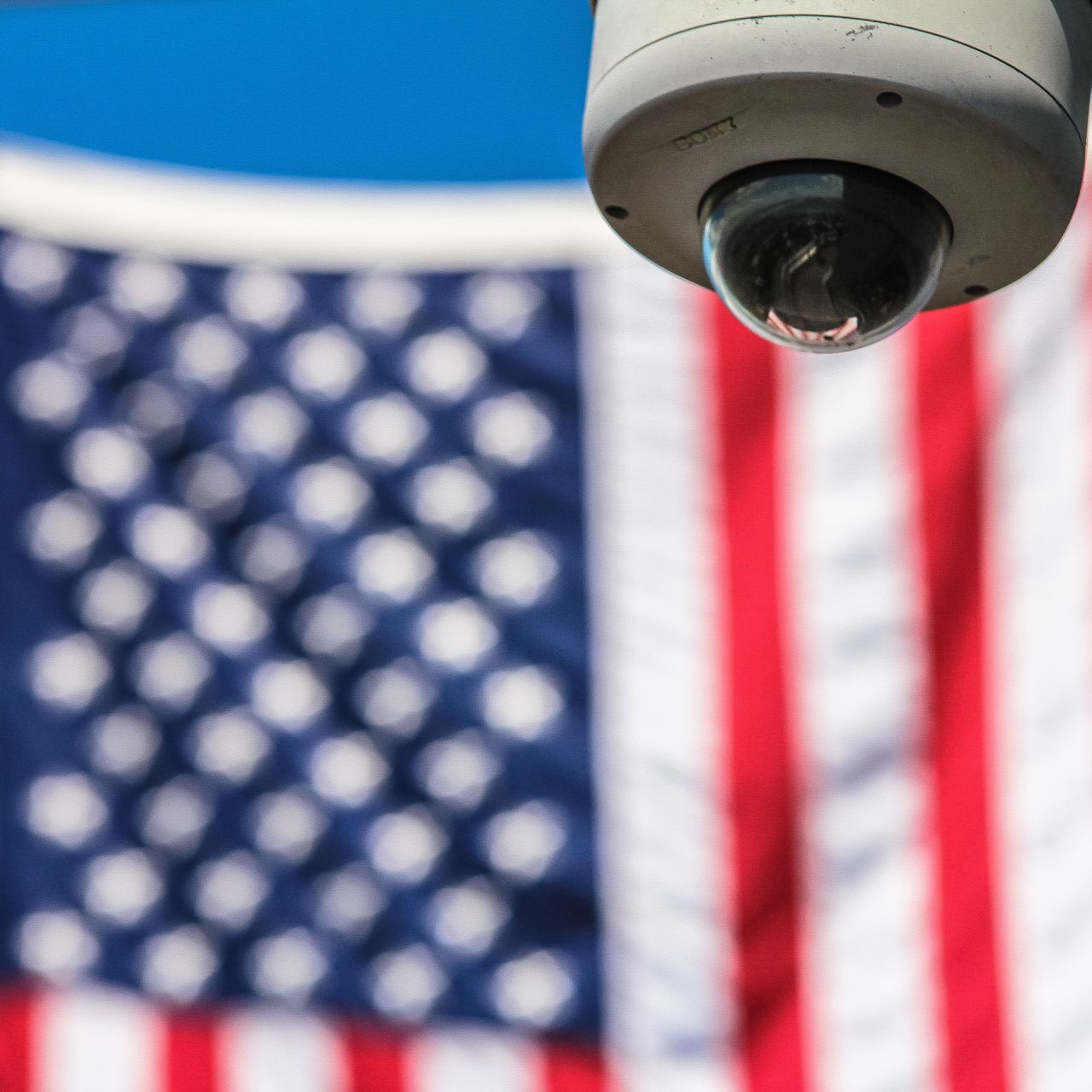 La bandiera a stelle e strisce degli Stati Uniti d'America sullo sfondo di una telecamera di videosorveglianza (Foto: Francesco Ungaro/Pexels)