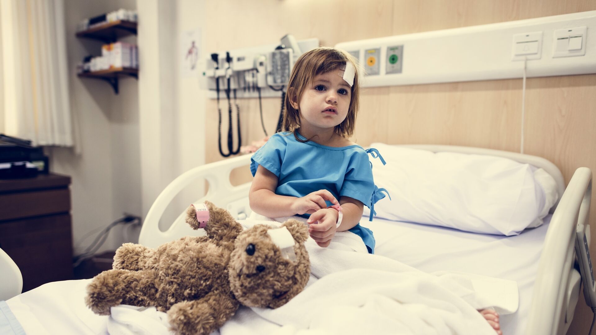 Assistenza sanitaria: una bambina ricoverata in ospedale seduta su un letto accanto al proprio orsacchiotto