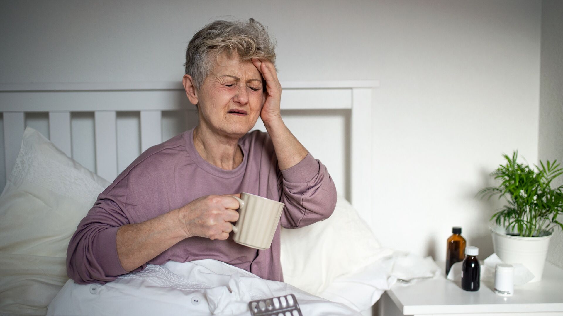 Assistenza sanitaria: un'anziana paziente afflitta da emicrania e alle prese con alcuni medicamenti in pastiglia