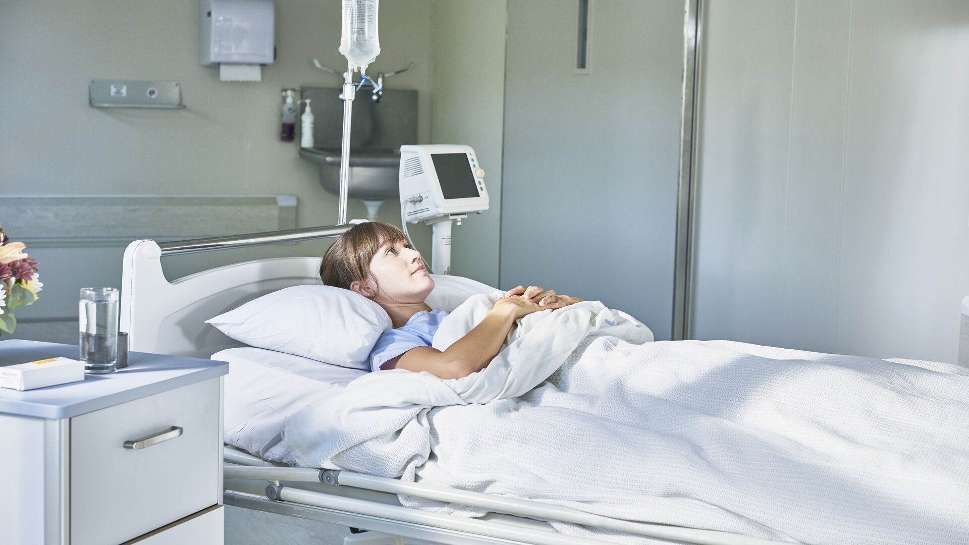 Assistenza sanitaria: un'ammalata giovane ricoverata in un letto d'ospedale e assorta nei propri pensieri