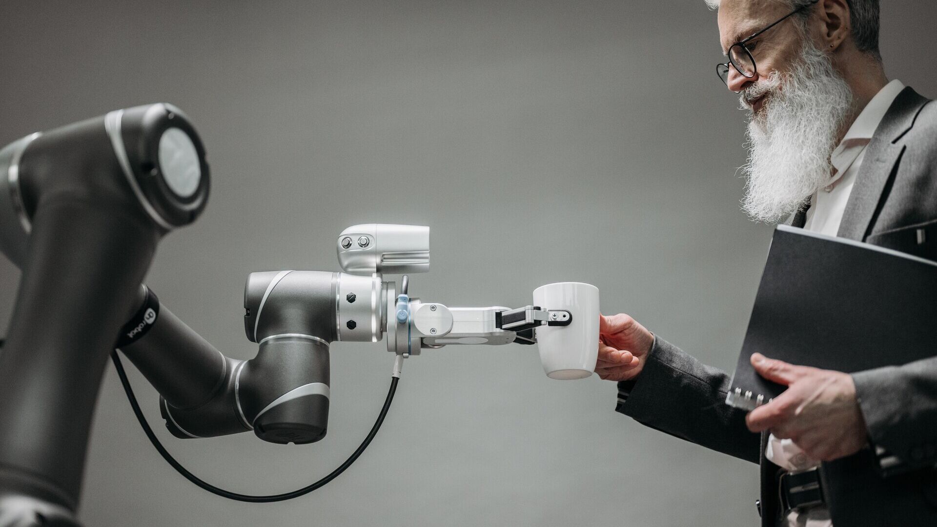 Futuro del lavoro: un uomo d'affari prende una tazza dalla mano artificiale di un robot: in futuro l'intelligenza umana e artificiale collaboreranno